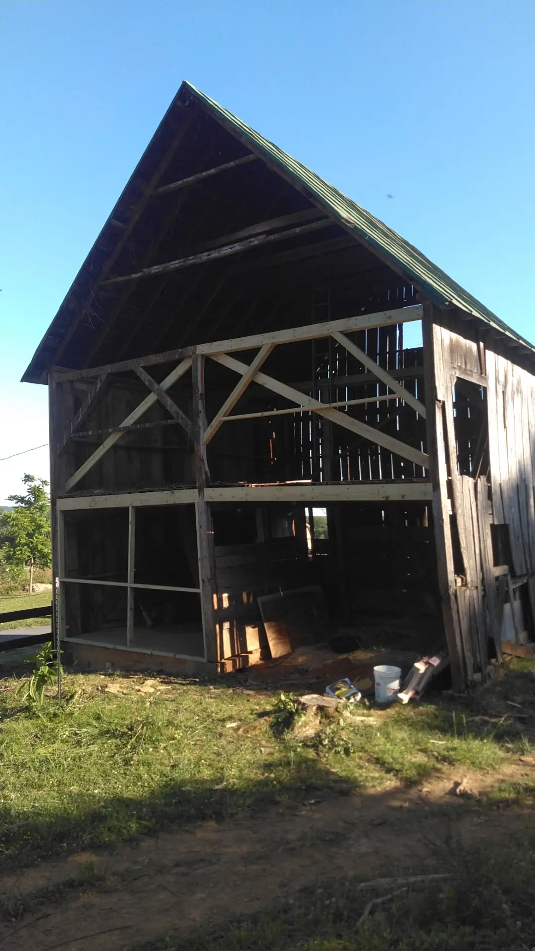 Barn with an open timber frame on one side and a green metal roof above.