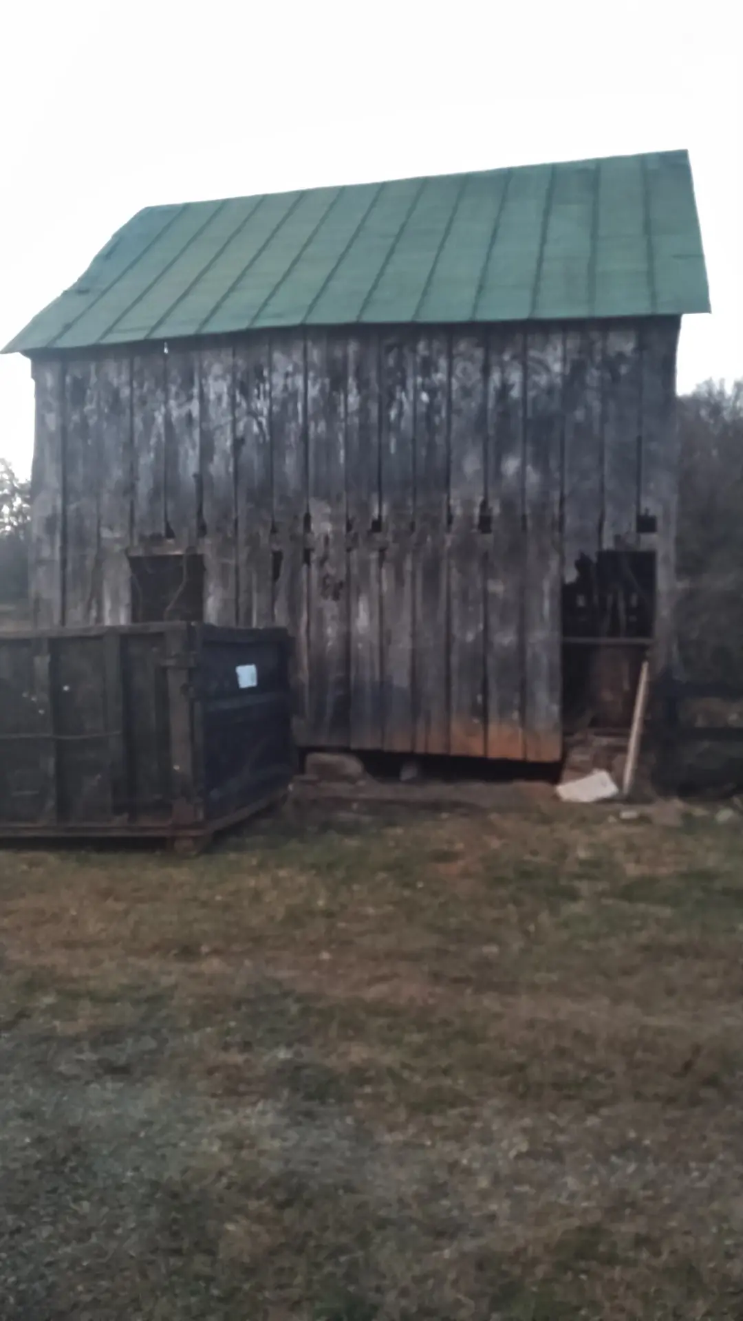 Tall barn with weathered gray siding and a green metal roof.