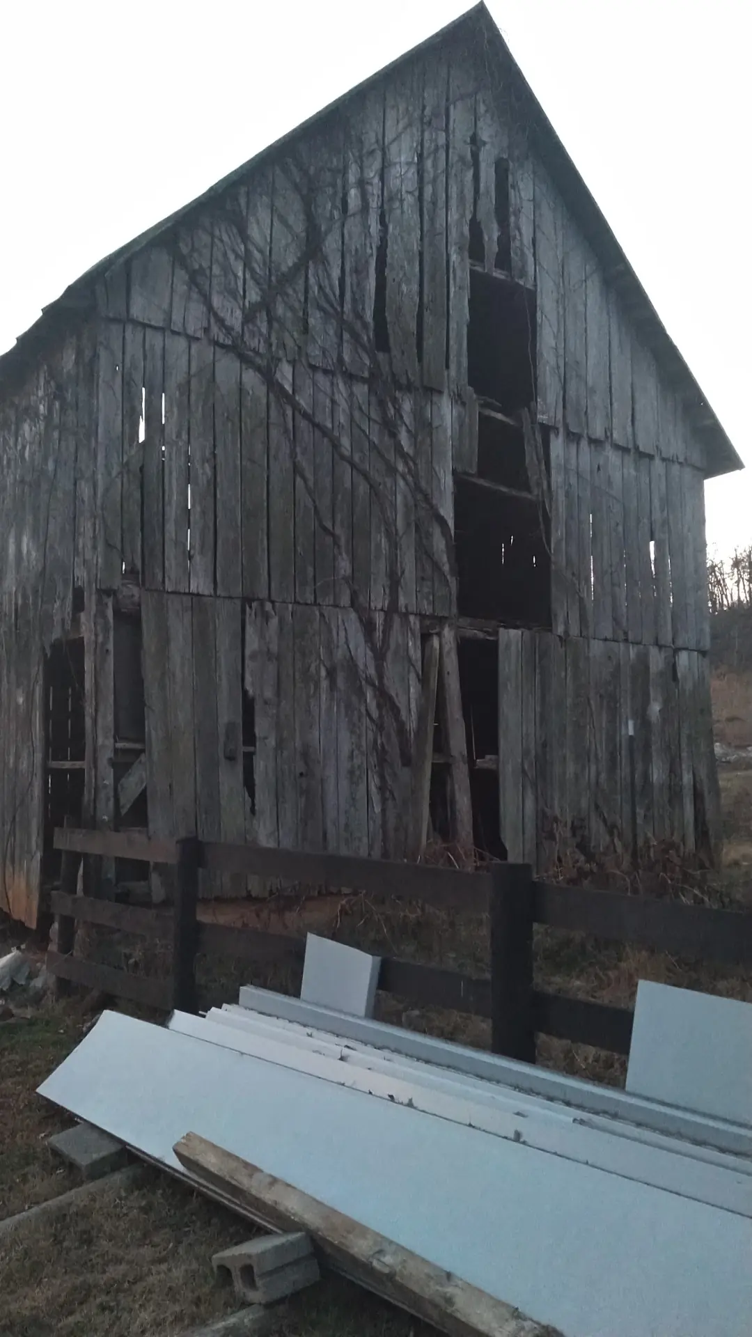Weathered gable end of a barn with stacked white trim boards in the foreground.