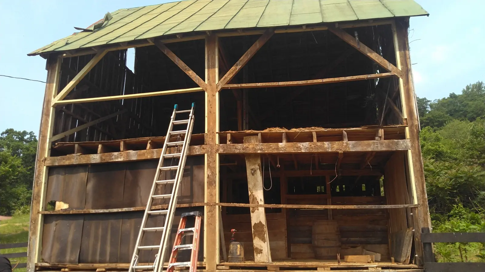 Open post-and-beam barn frame with a ladder and a green metal roof overhead.
