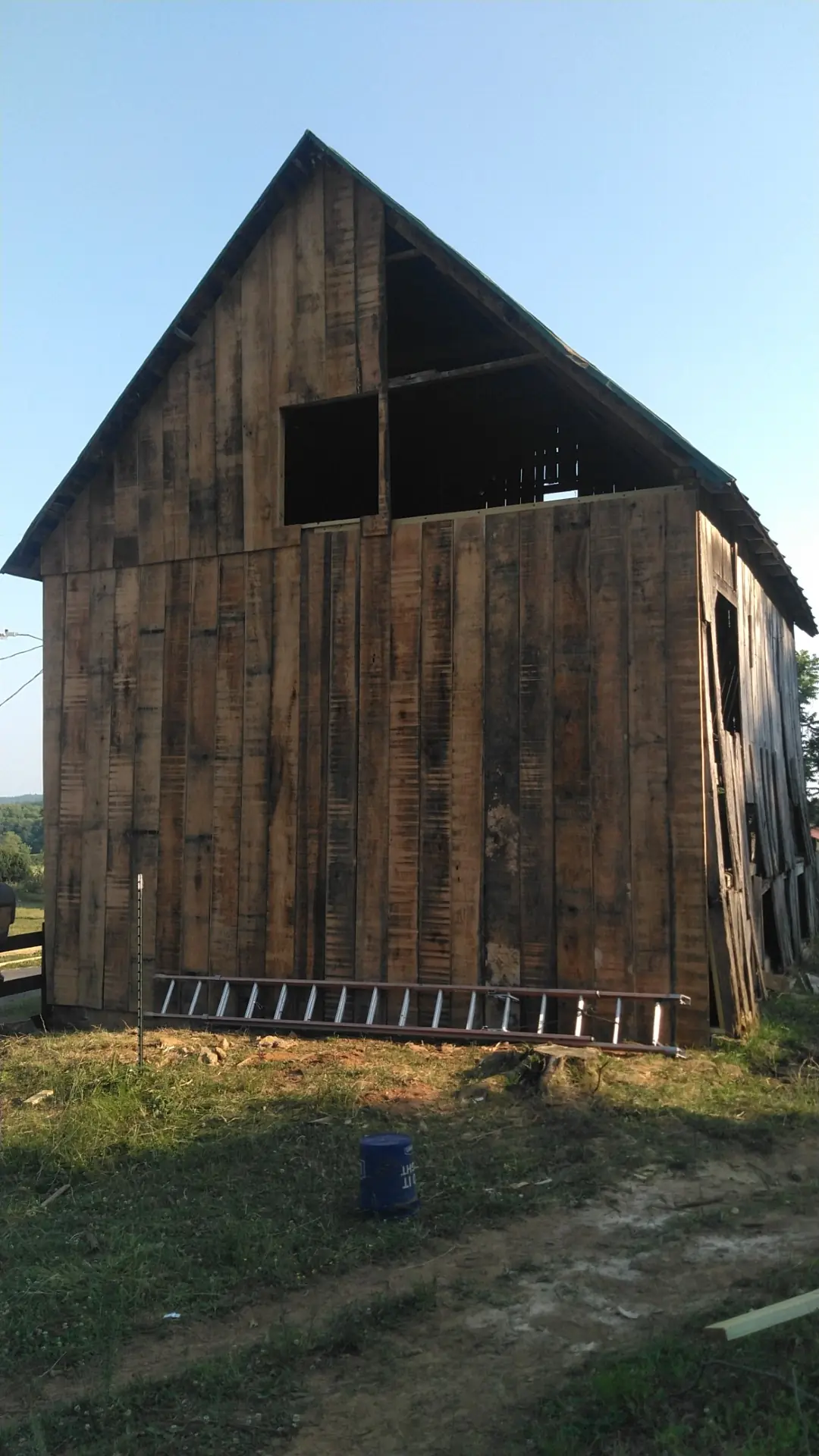 Side of the barn with new siding, an opening and a ladder against it.