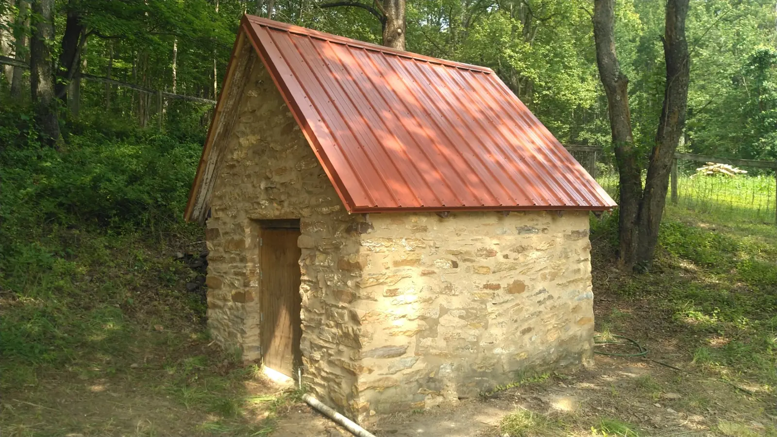 Small stone building with a red standing seam roof in the woods.