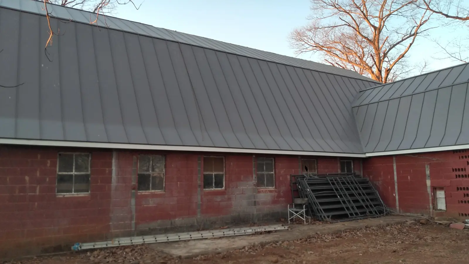 Brick wing with a long gray standing seam roof and a steel stair at the side.