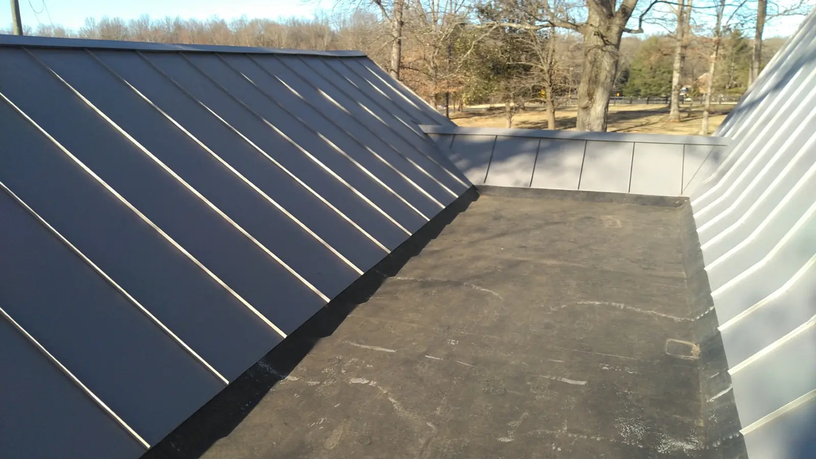 Dark standing seam metal on either side of a flat membrane valley.