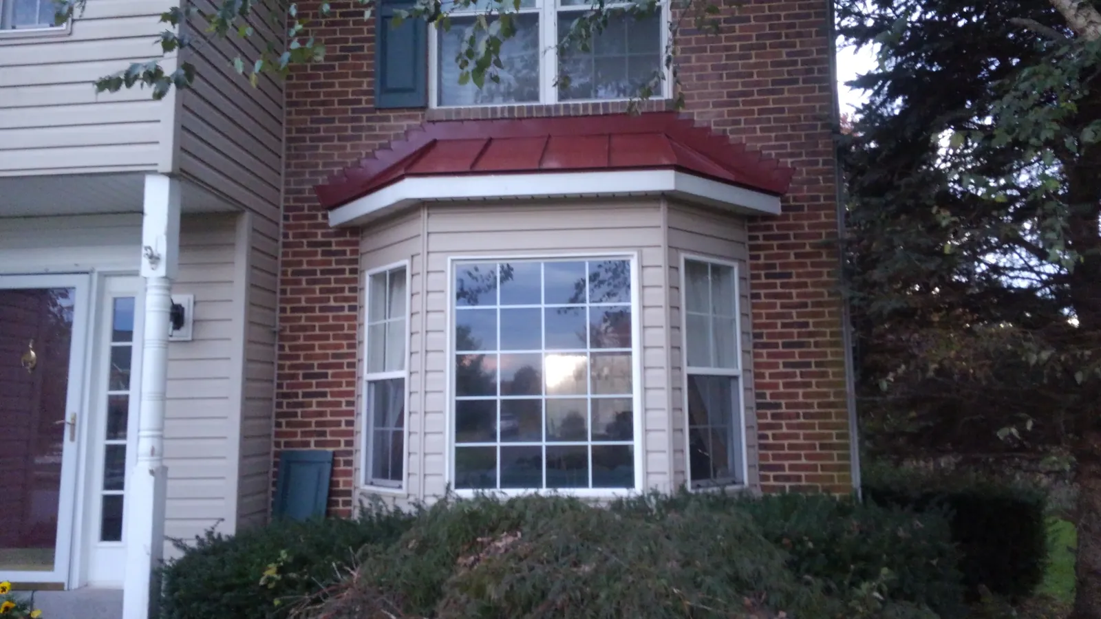 Brick home with a bay window capped in a red standing seam roof.