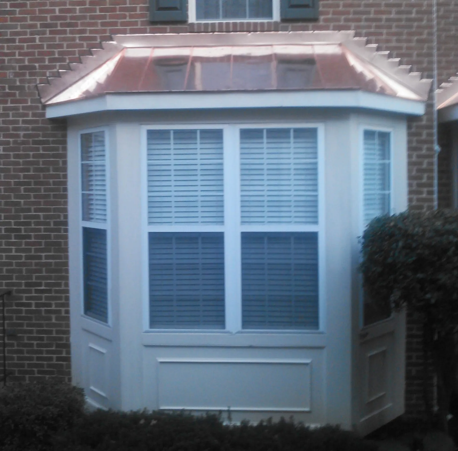 White-trimmed bay window under a copper roof set into a brick wall.