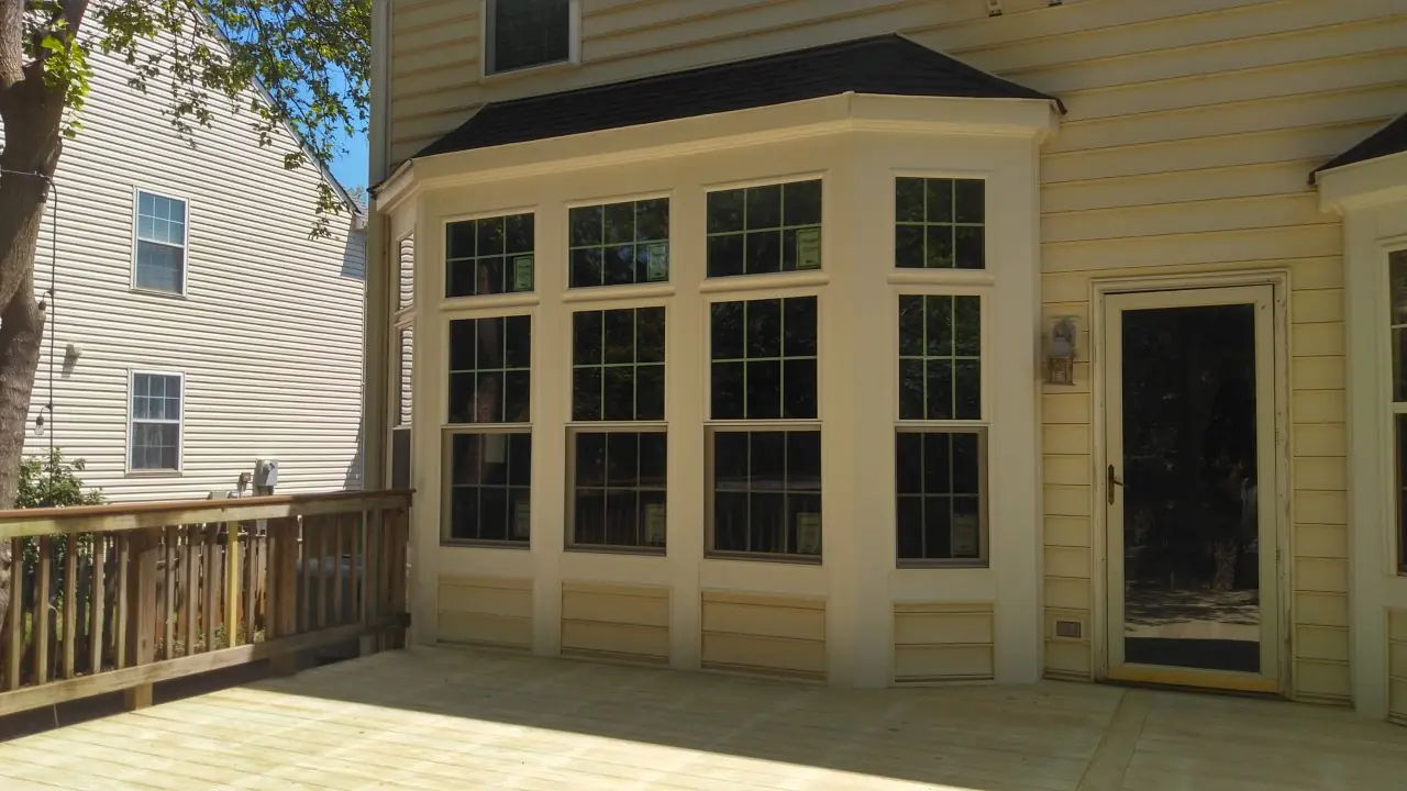 Bay window with a dark roof over it, white trim and a screen door beside.