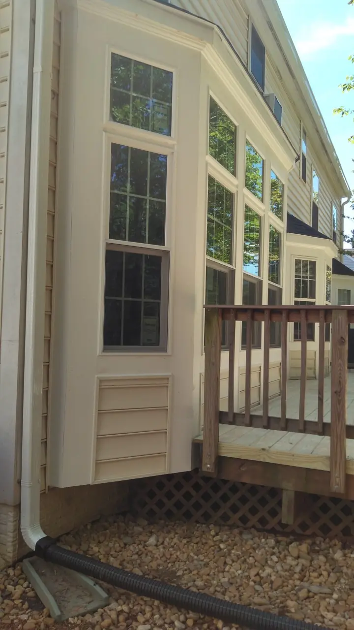 Corner of the bay with trim, a downspout and a deck railing.