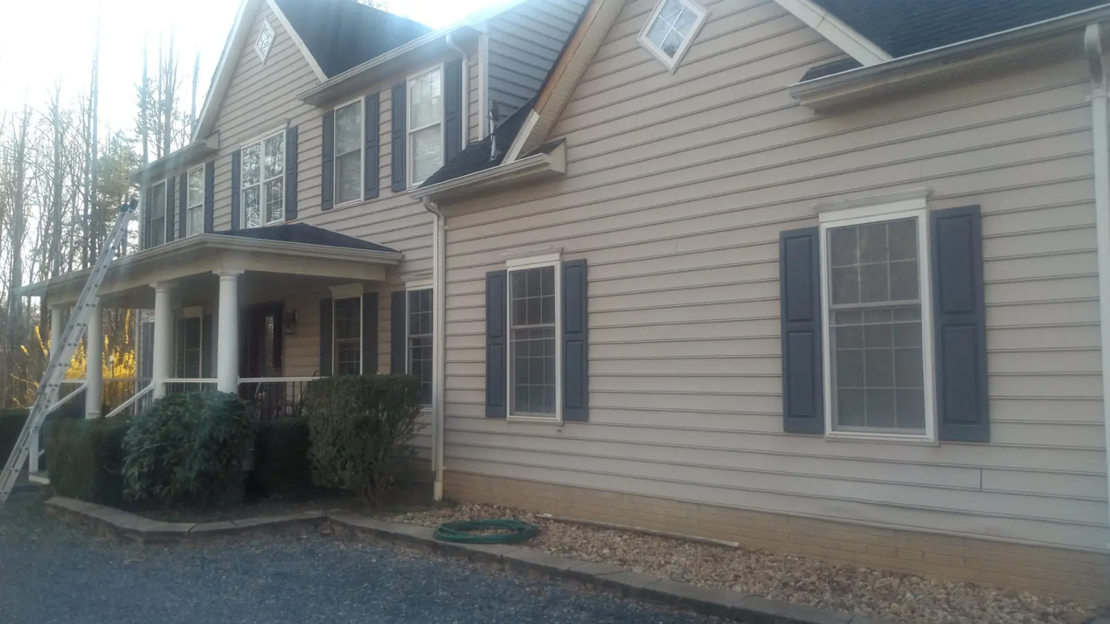 Side of a beige home with dark shutters, tall windows and the porch corner.