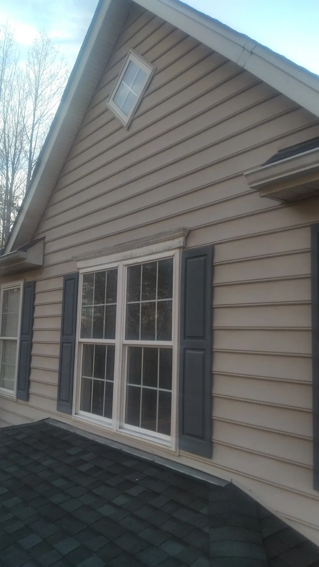 Gable window with shutters above new shingles.