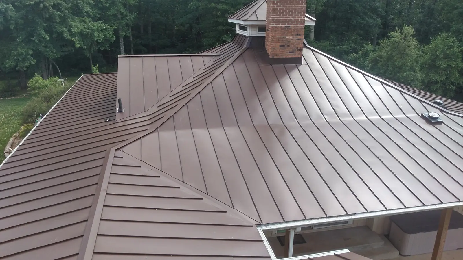 Bronze standing seam hip roof with a cupola and brick chimney over a deck.