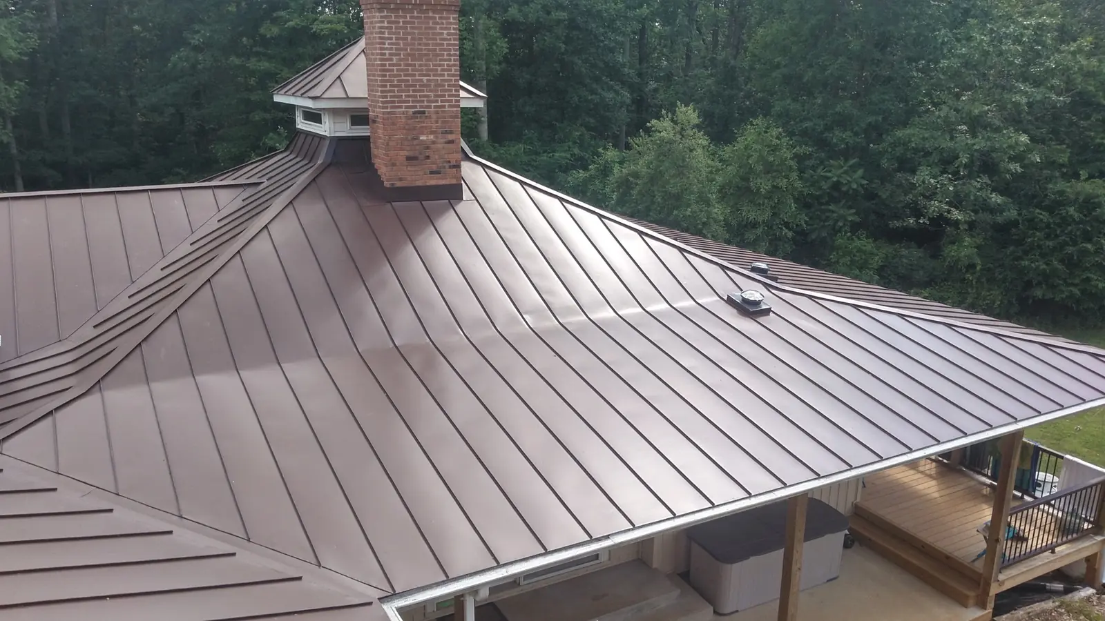 Bronze standing seam roof with hips, valleys and a brick chimney.
