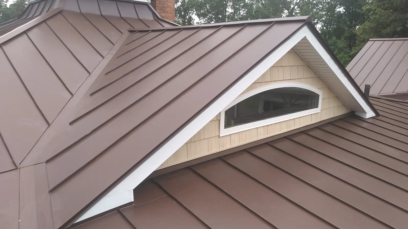 Bronze standing seam wrapped around an arched dormer window.
