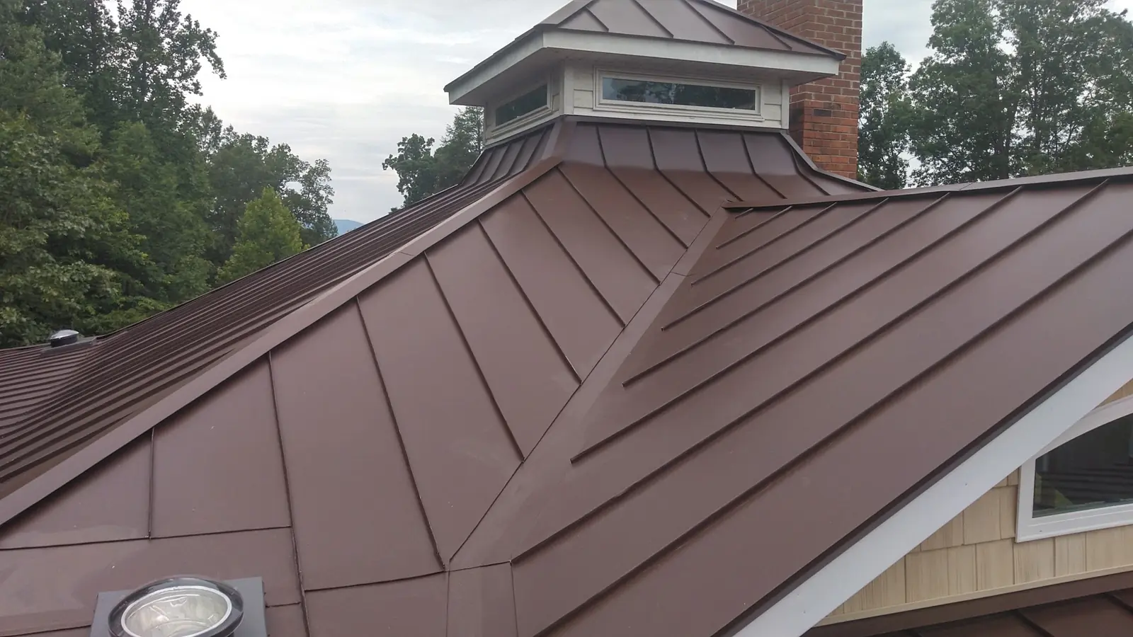 Bronze standing seam with a cupola, a chimney and a dormer window at the edge.
