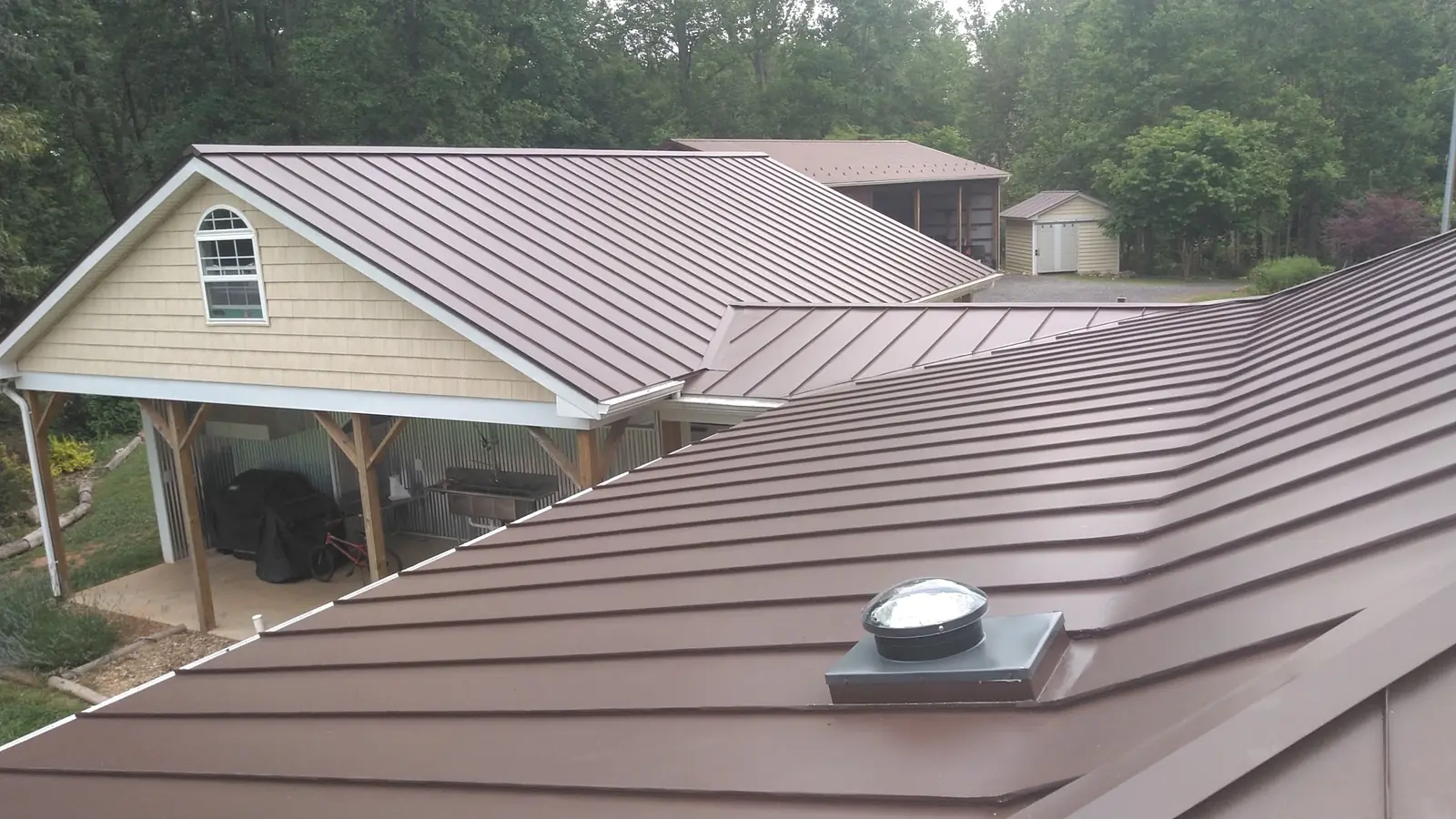 Bronze standing seam roof over an addition with a yellow-sided porch gable.