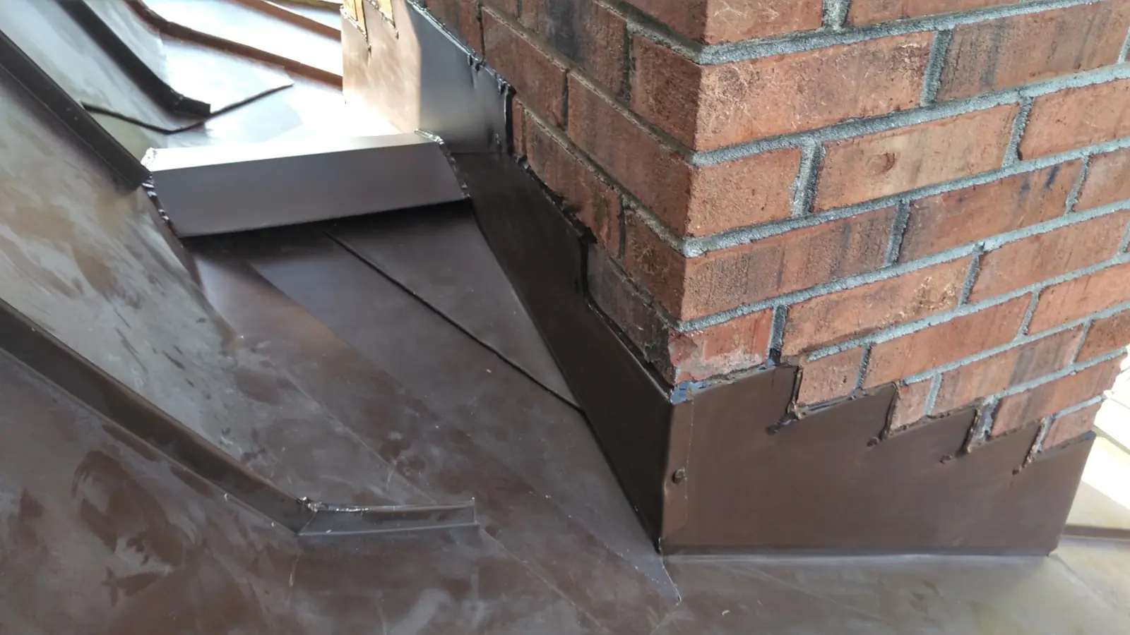 Brown metal flashing at a brick chimney with stepped counterflashing.
