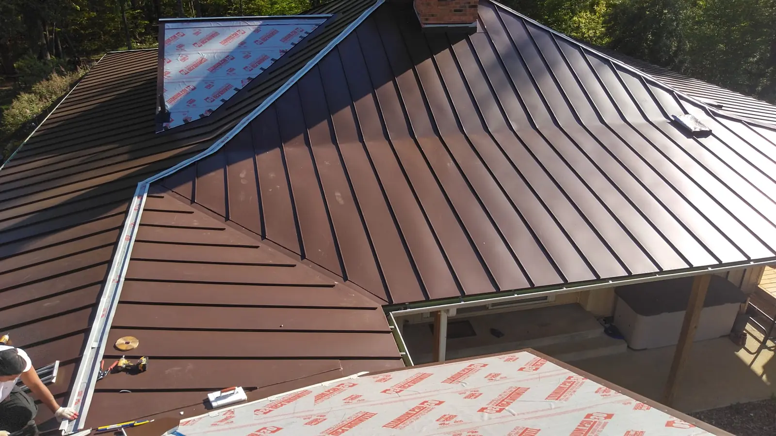 Brown standing seam valley and hip over red-printed underlayment with a person at the eave.