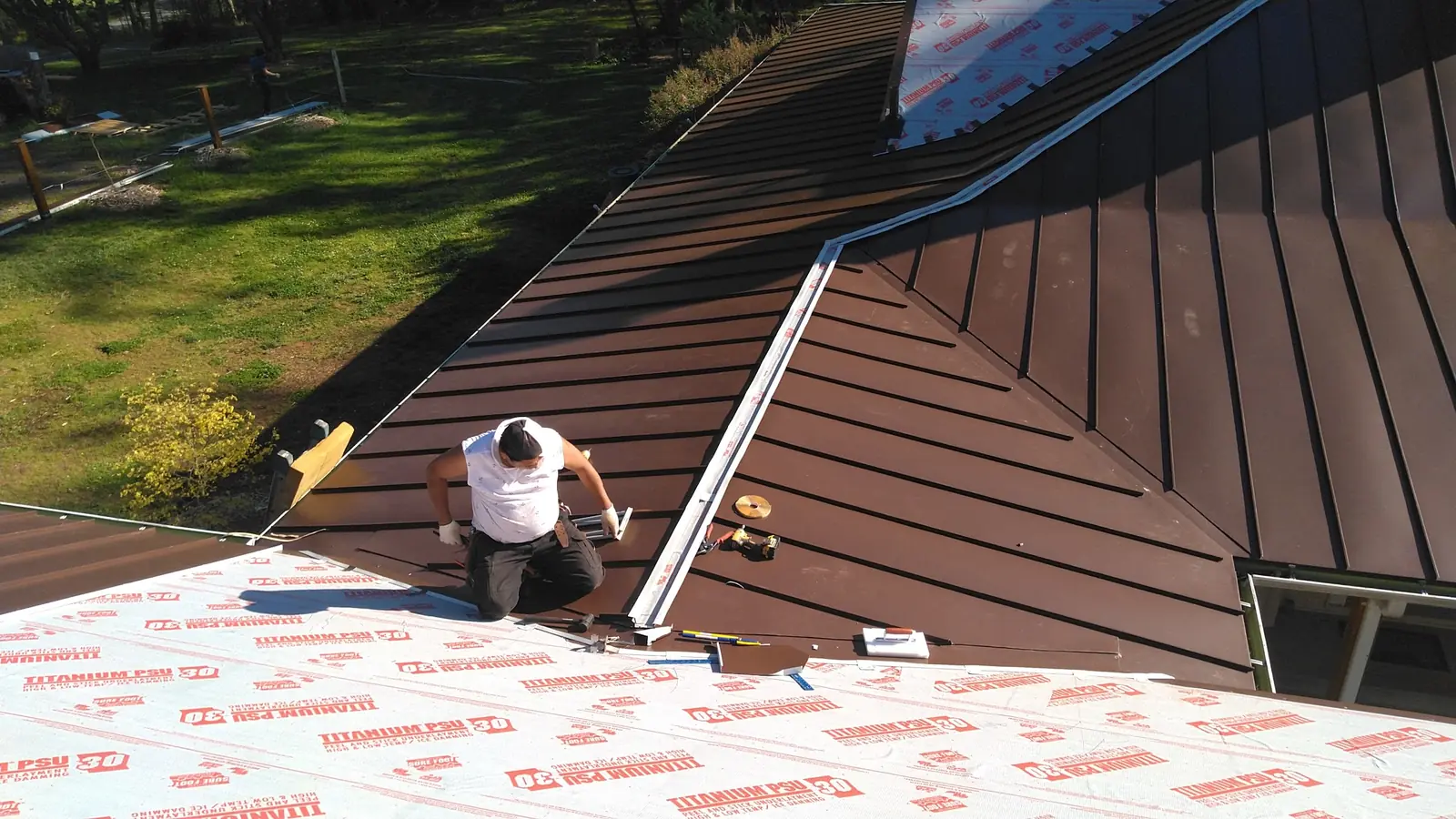 Crew member fastening brown panels beside a skylight opening on underlayment.