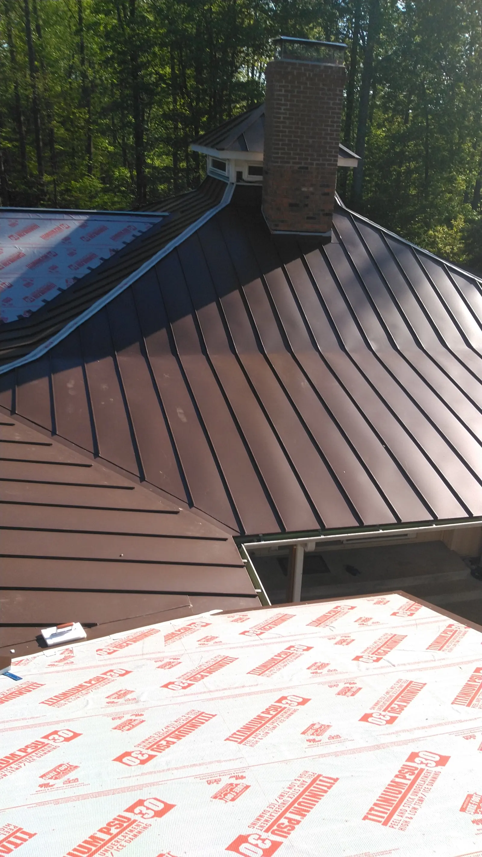 Brown standing seam panels near a skylight opening with underlayment beside.