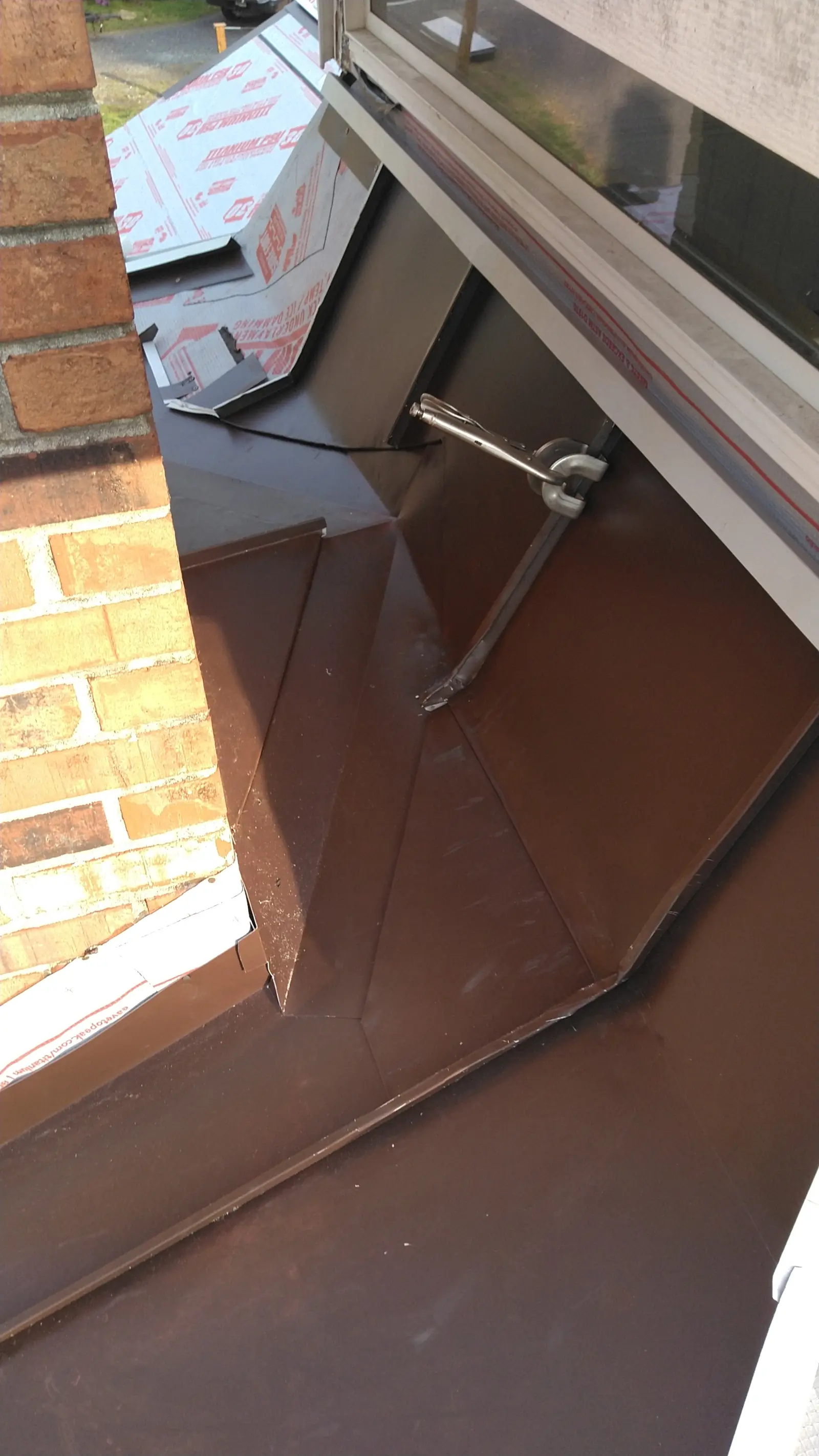 Brown metal flashing tied into a brick chimney.