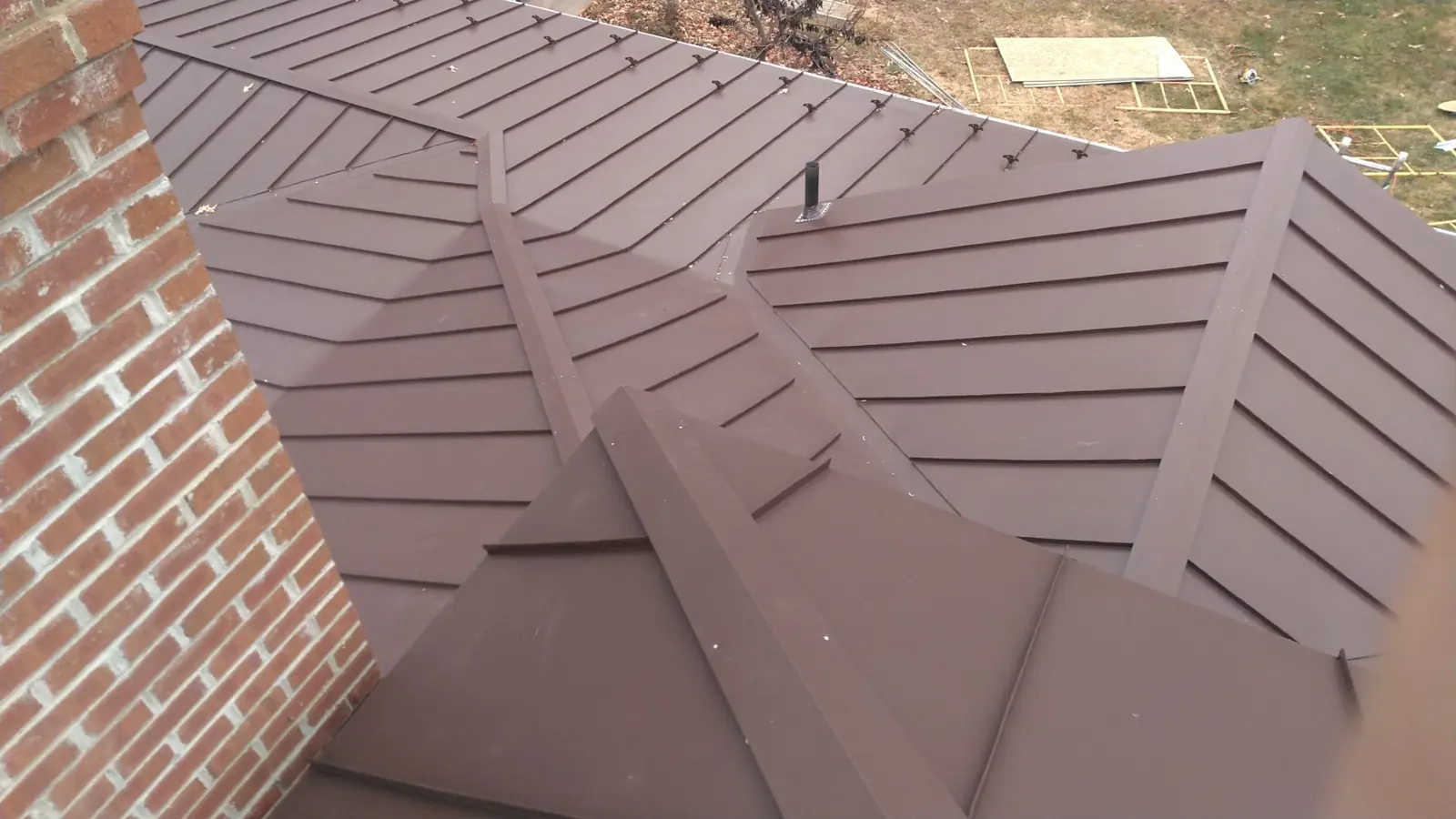 Brown standing seam hip and flashing beside a brick wall.