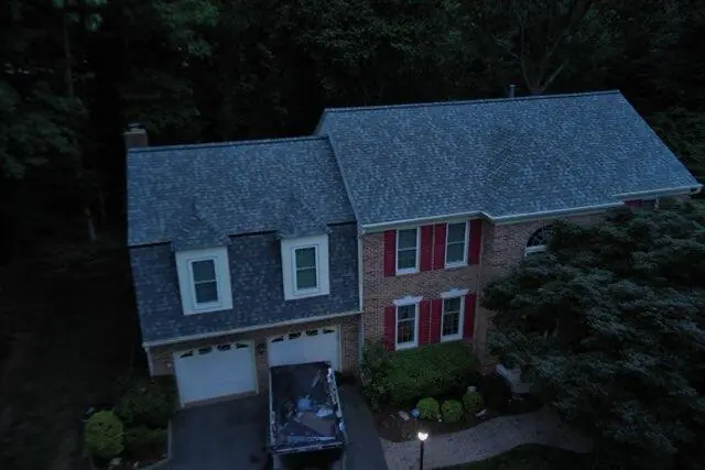 Aerial view of a brick home with red shutters, a garage and a blue-gray shingle roof.