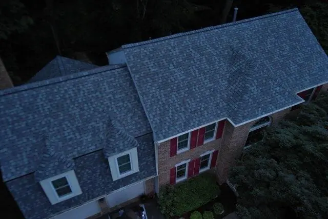 Aerial view of the shingle roof ridges and valleys over a brick home with red shutters.