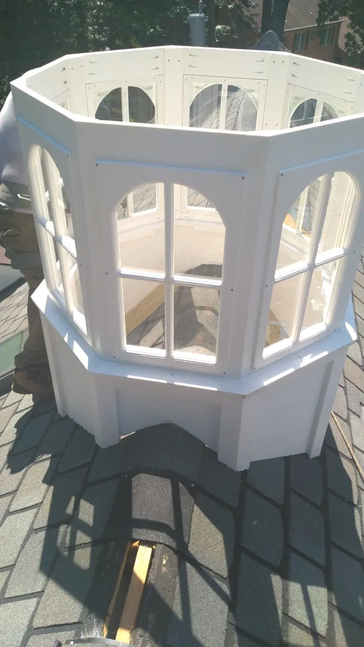 Closeup of a white octagonal cupola with arched louvers on a gray shingle roof.
