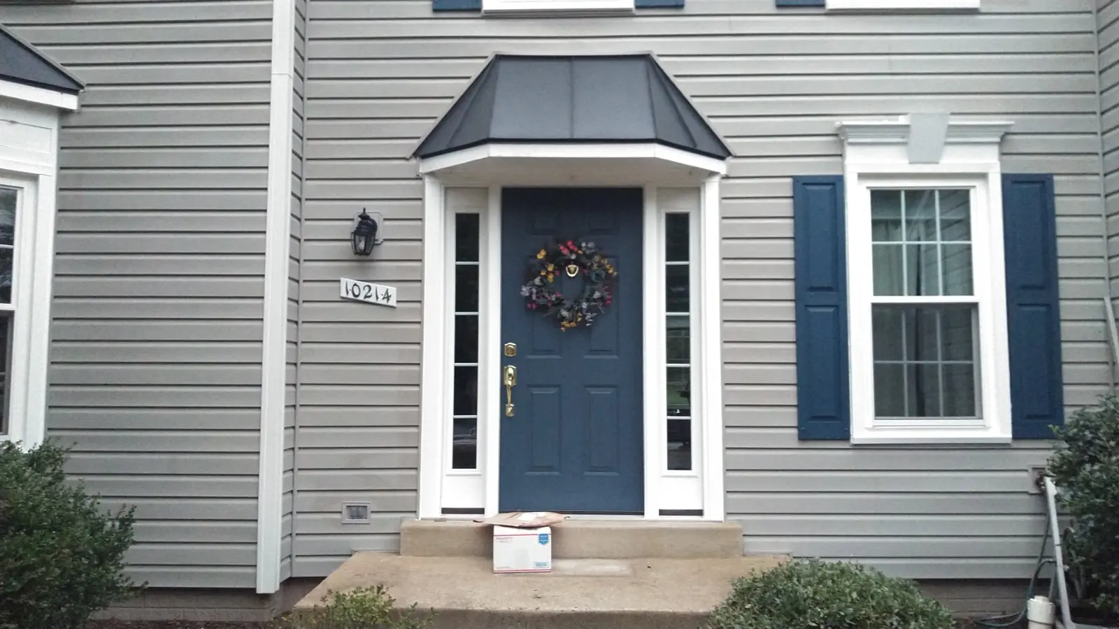 Dark gray standing seam hood over a blue front door with white trim and blue shutters.