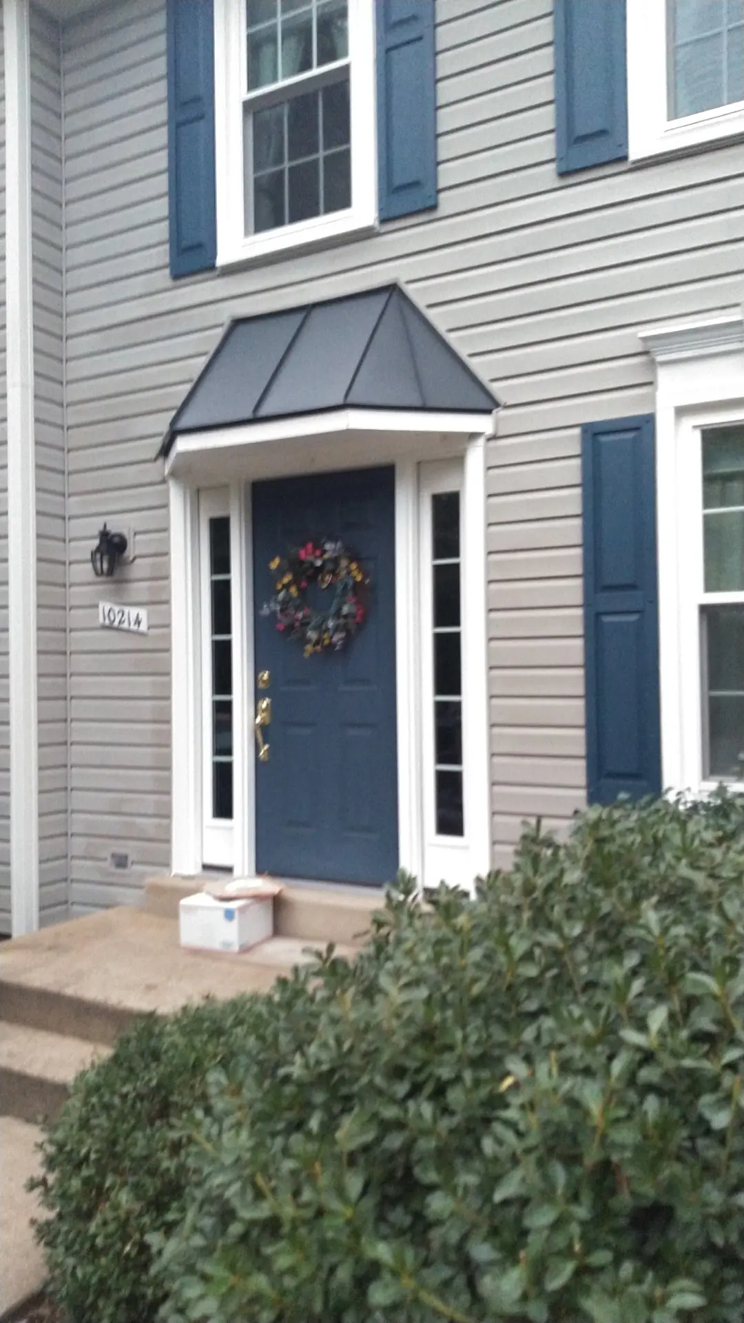 Blue front door with a dark metal roof above it and blue shutters.