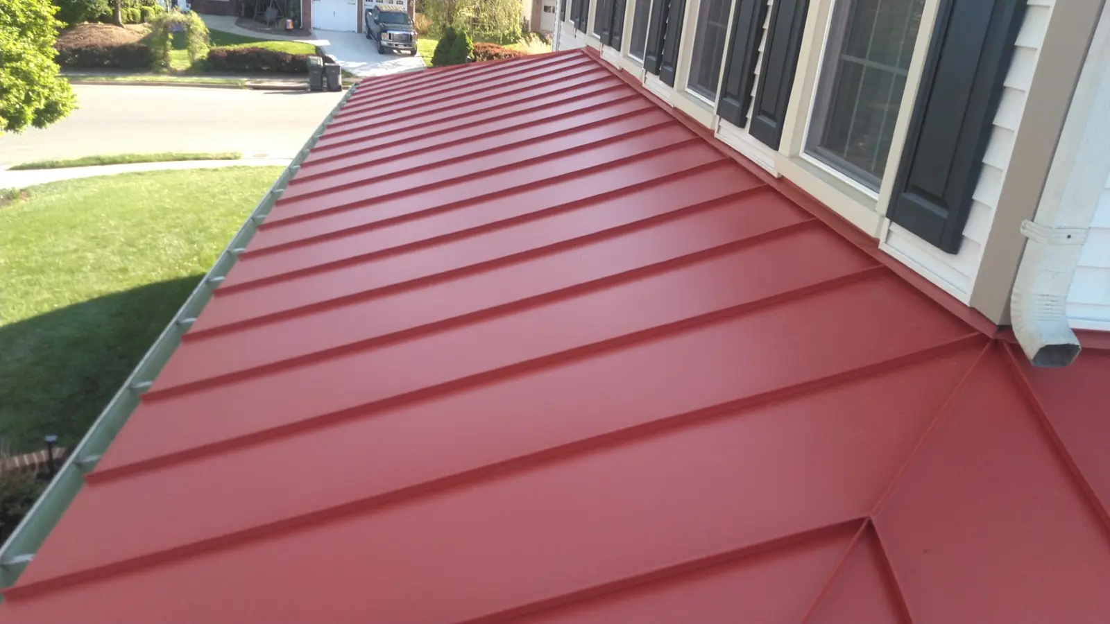 Deep red standing seam roof beside siding and windows with a gutter along the eave.
