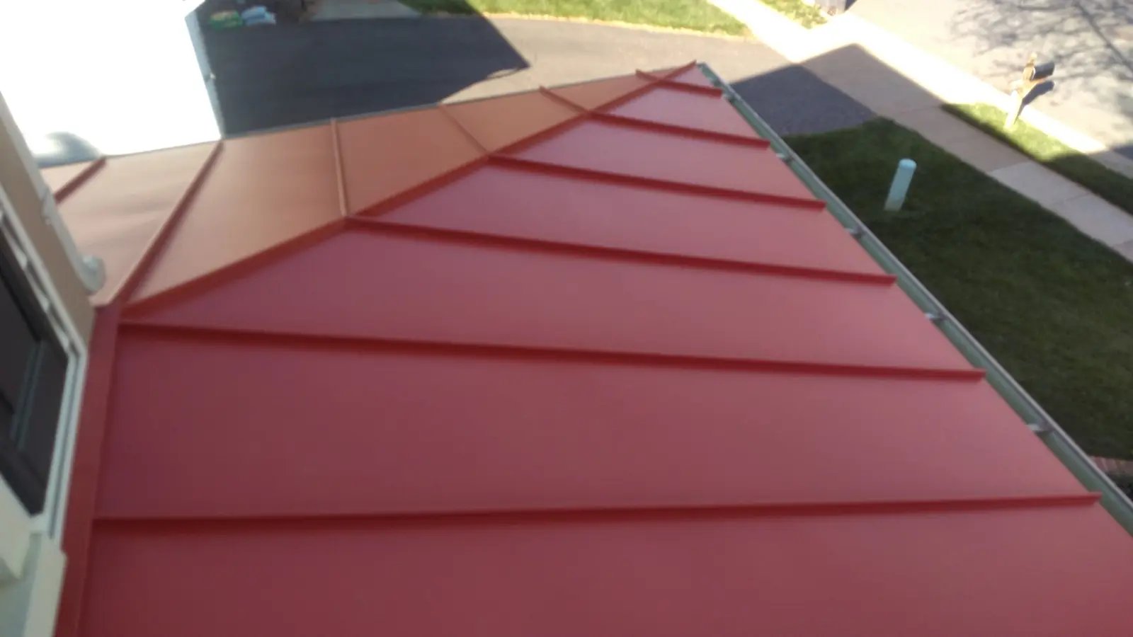 Deep red standing seam hip and ridge with a gutter and street below.