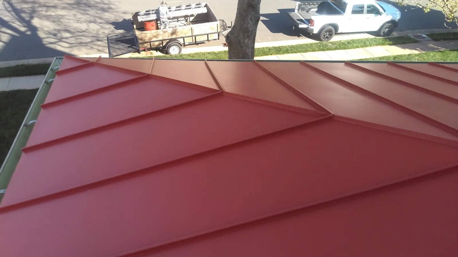 Deep red standing seam roof with a hip and a trailer in the driveway below.