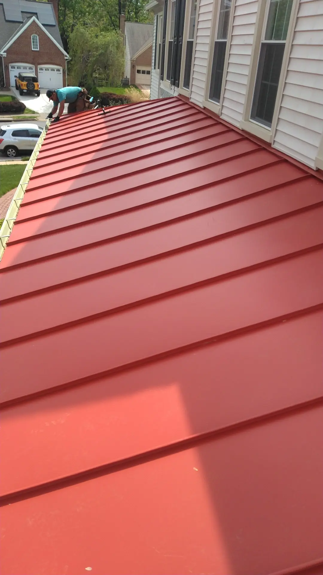 Deep red standing seam roof beside siding and windows, portrait view.