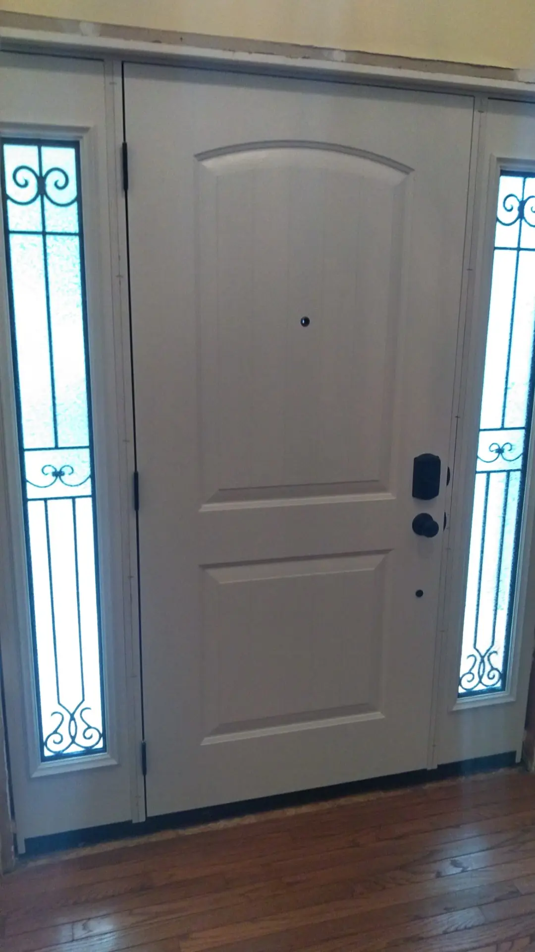 White entry door with decorative glass sidelights in a hall with wood floor.