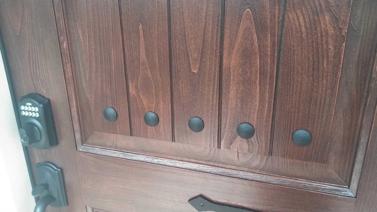 Closeup of a stained wood door panel with decorative studs and a keypad lock.