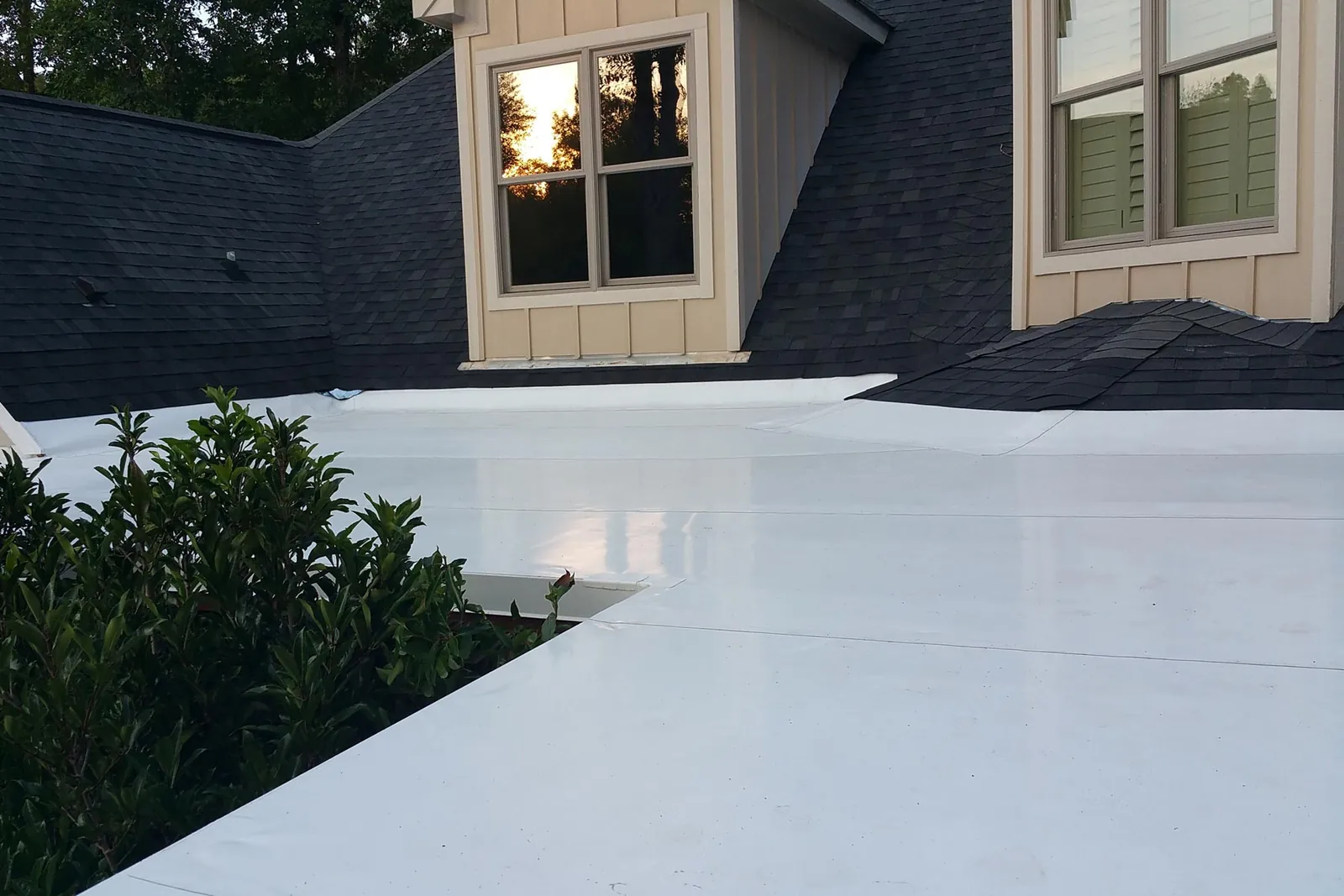 White single-ply flat roof membrane beside a dark shingle roof and tan siding.