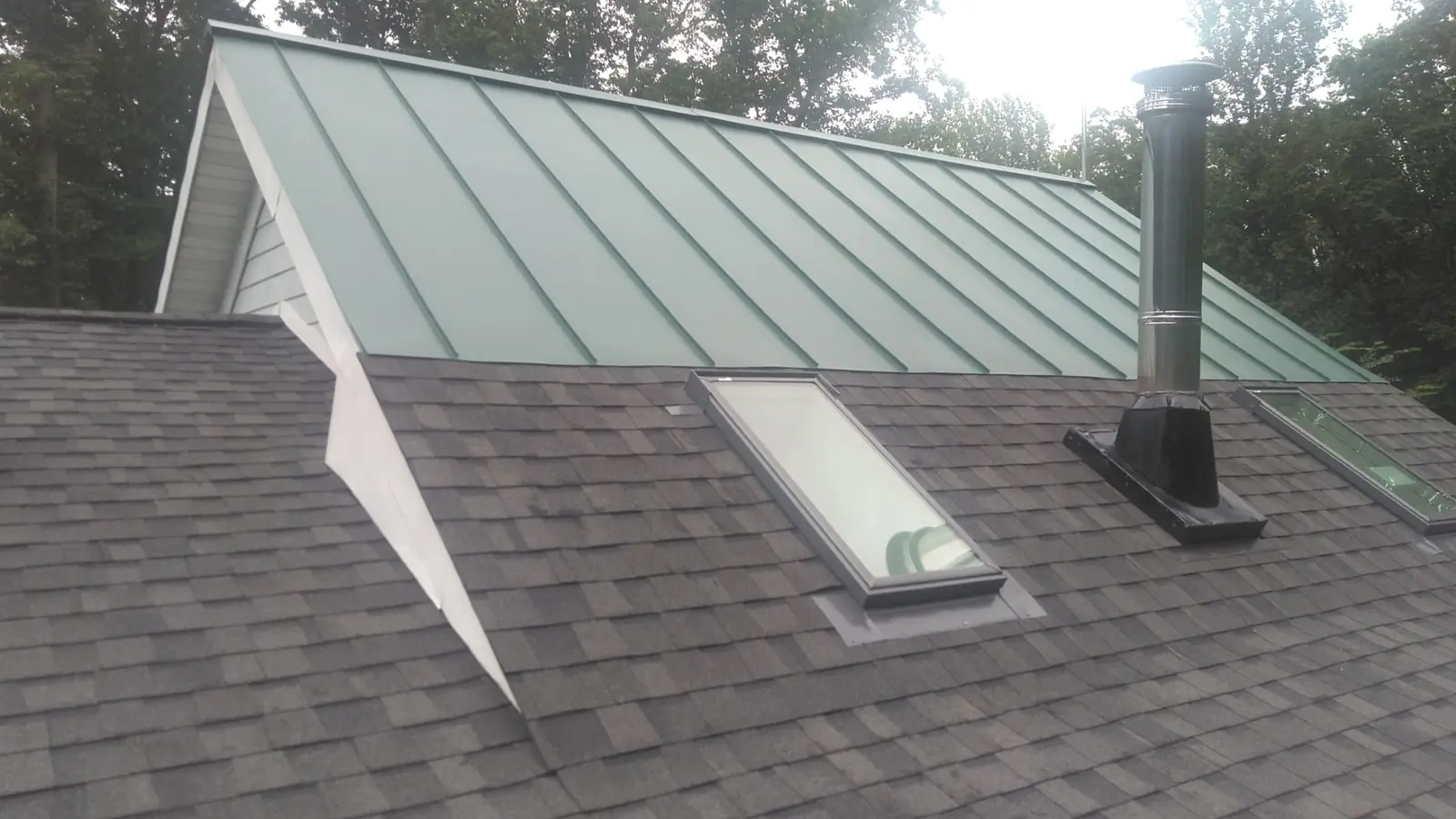 Forest green standing seam gable beside gray shingles and a skylight.
