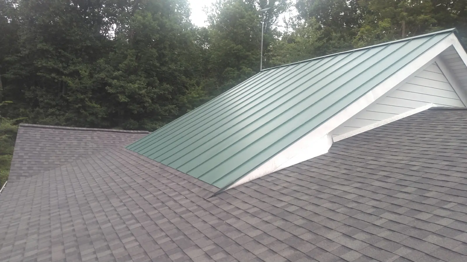 Forest green standing seam gable with white trim beside gray pewterwood shingles.