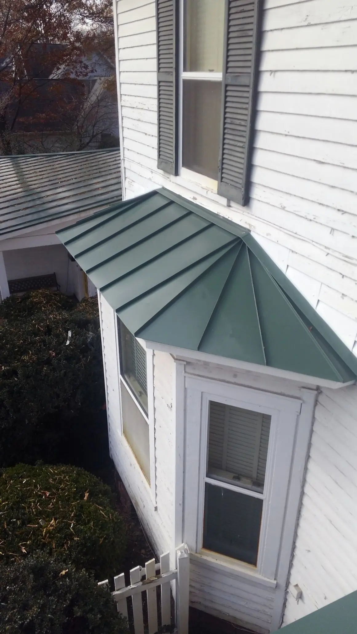 Forest green metal roof over a bay window on a white house.
