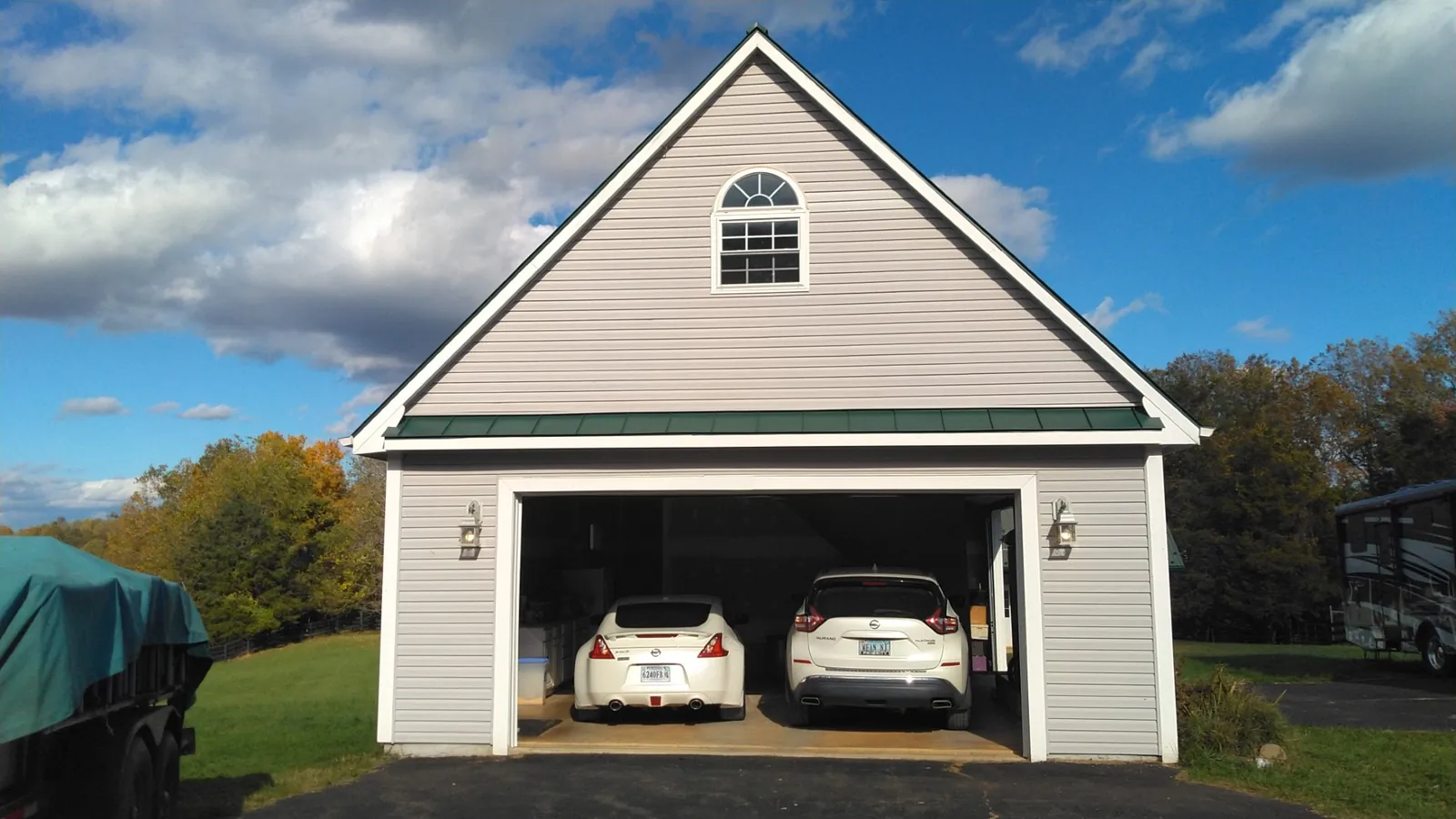Detached two-car garage with tan vinyl siding, a gabled roof and green trim.