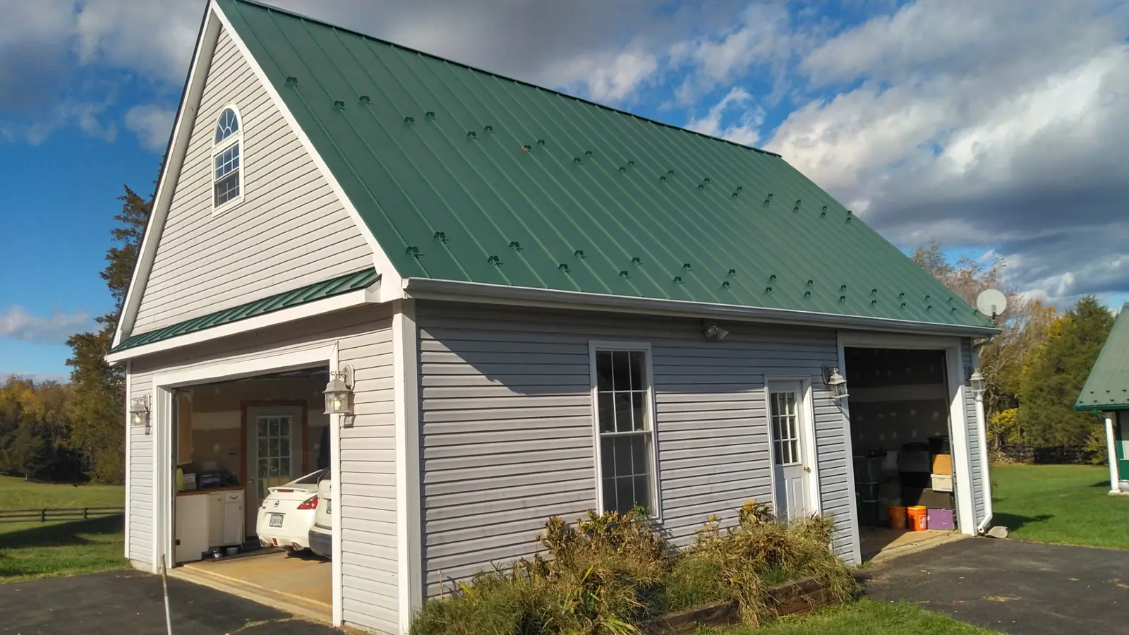 Detached garage with a new green standing seam roof, white trim and an open garage bay.
