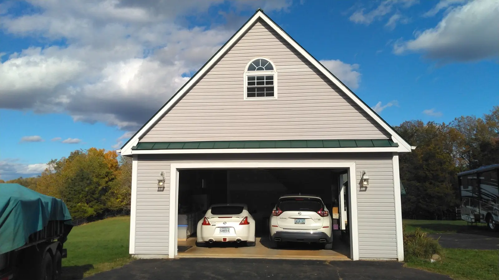 Front gable of a two-car garage with a green metal roof, open doors and two cars.