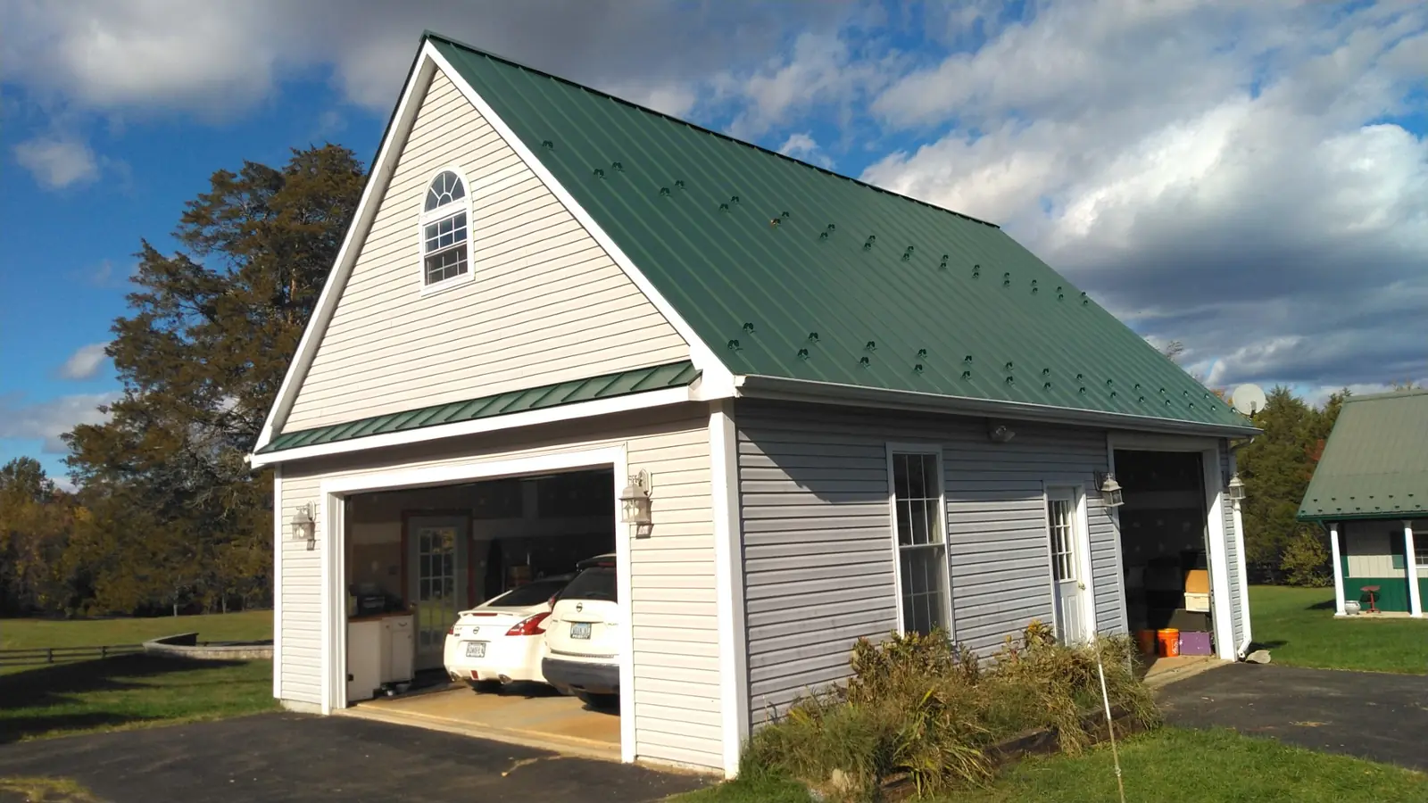 Garage with a green metal roof and a car parked inside under a blue sky.