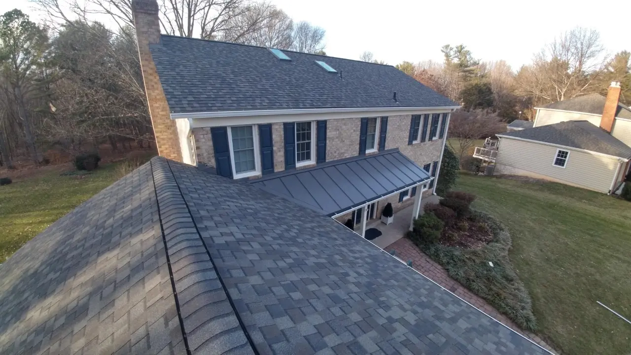 Brick colonial with dark shingles on the main roof and gray metal over the porch.