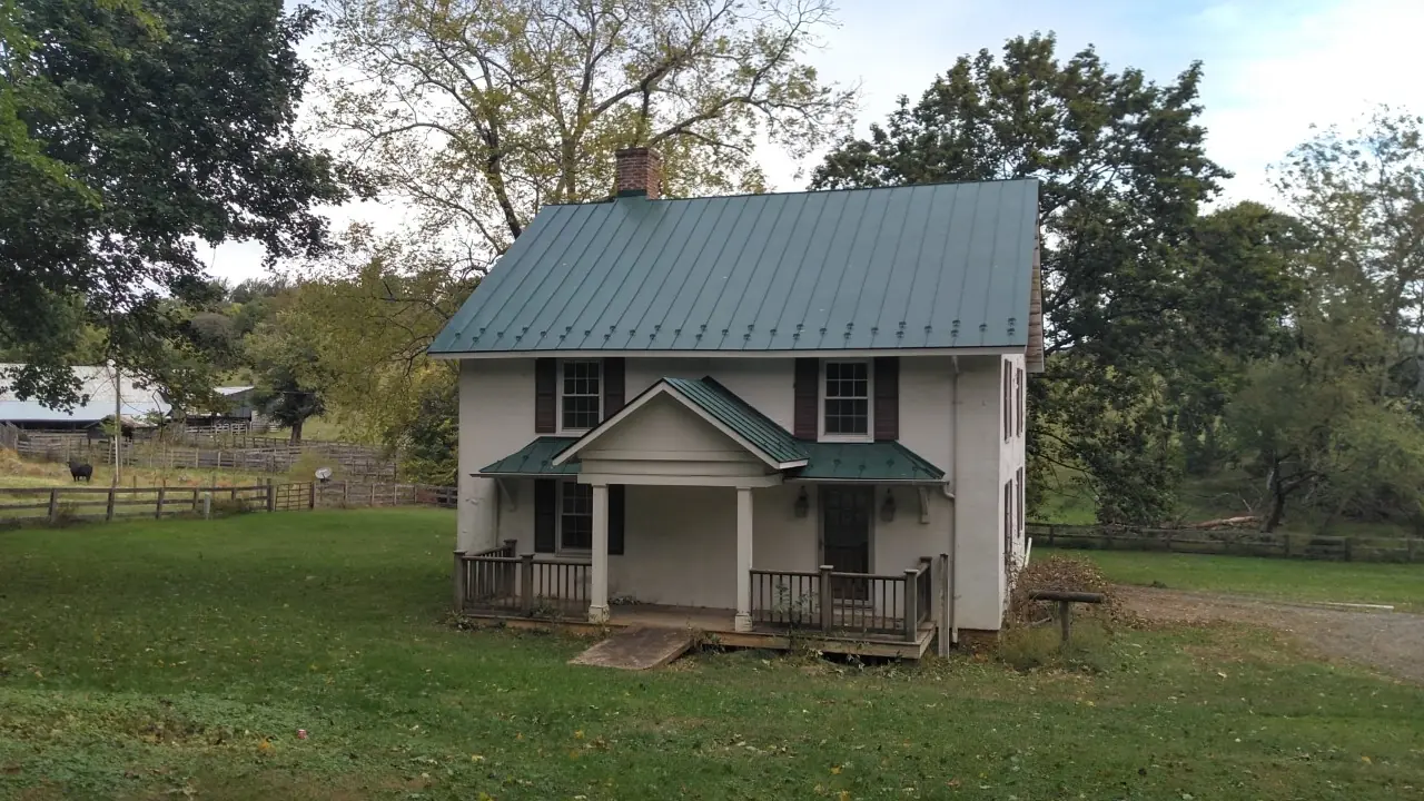 White farmhouse with a green standing seam roof and porch roofs on a grass yard.