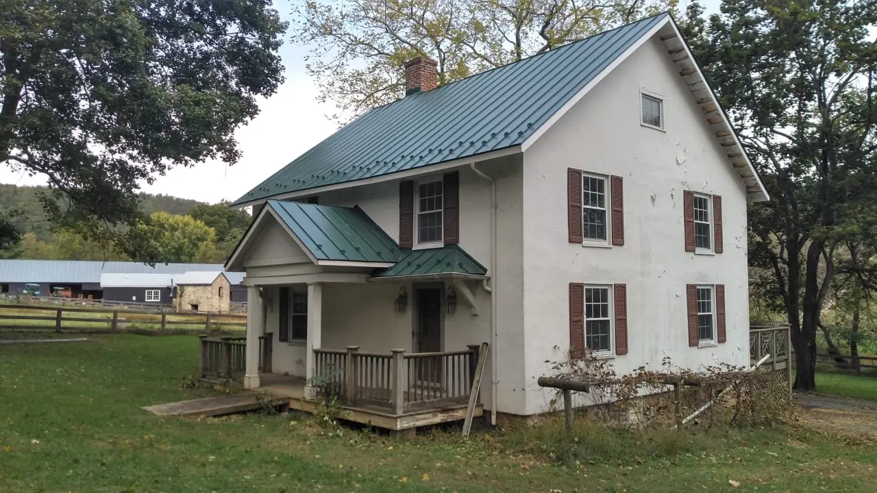 White farmhouse with green metal roofs over the main house and porch.