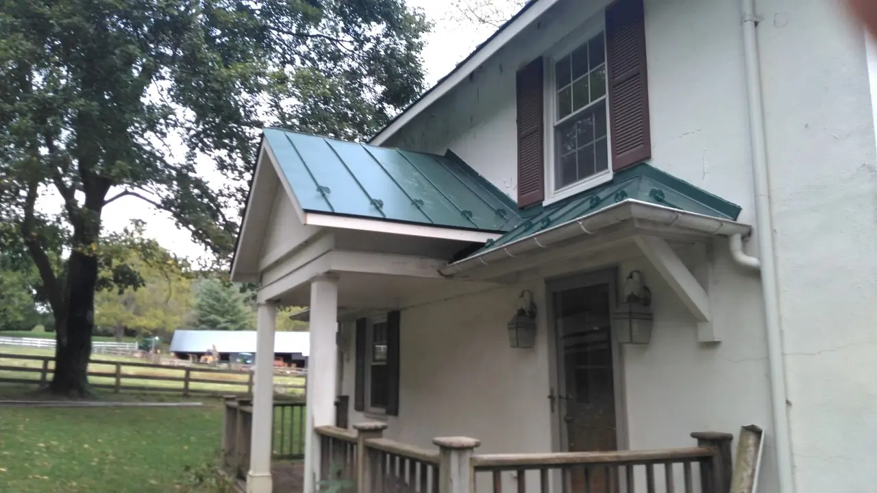Green standing seam porch roof with white columns and a wooden railing.