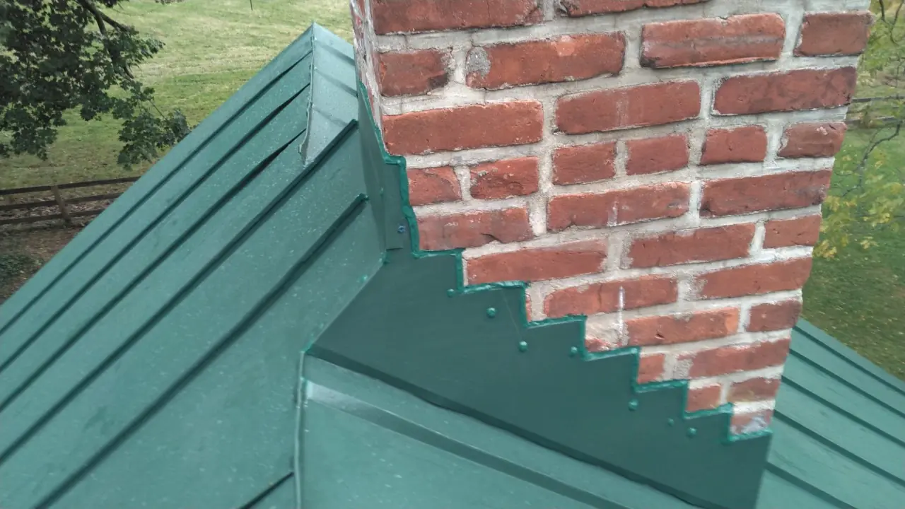 Green standing seam roof with saw-tooth counterflashing at a brick chimney.