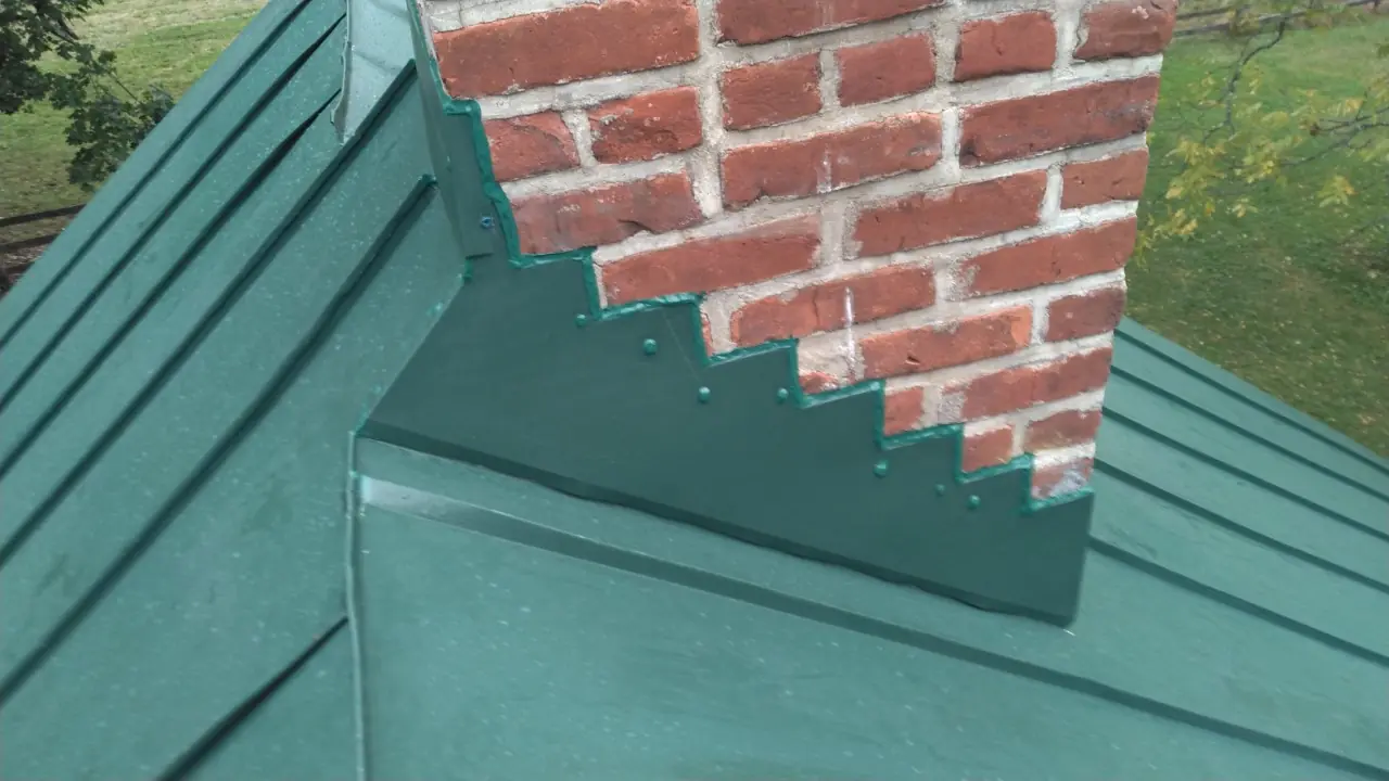Green metal roof meeting a brick chimney with stepped flashing.